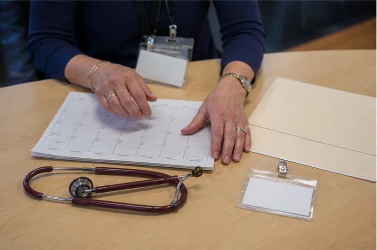 A close view of a capacity calendar, visitor badge, and stethoscope on a clinic worktable
