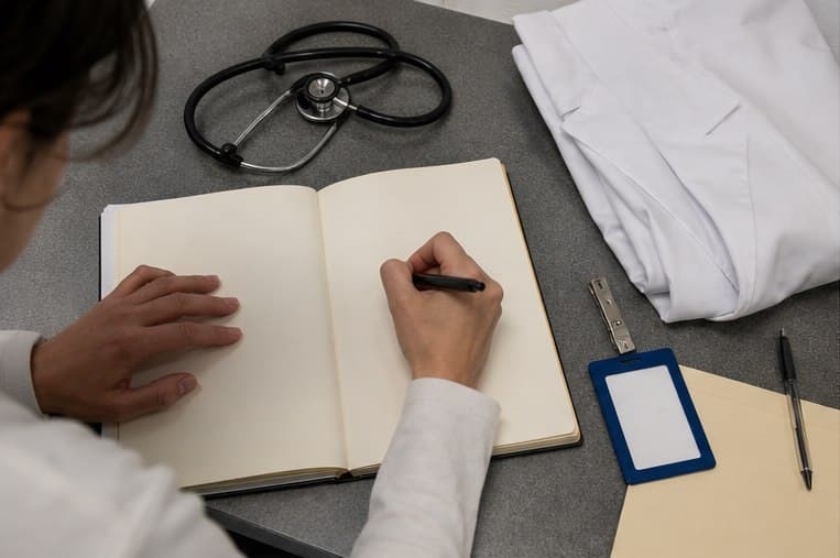 An open preparation guide beside a stethoscope, short white coat, and visitor badge